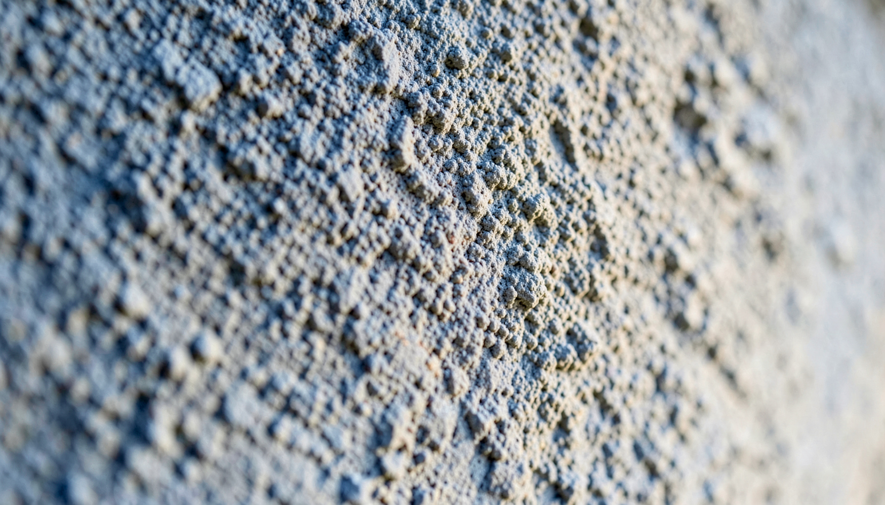 Textura de un muro de concreto en tonos grises y beige, con luz natural suave que resalta la superficie ligeramente rugosa.